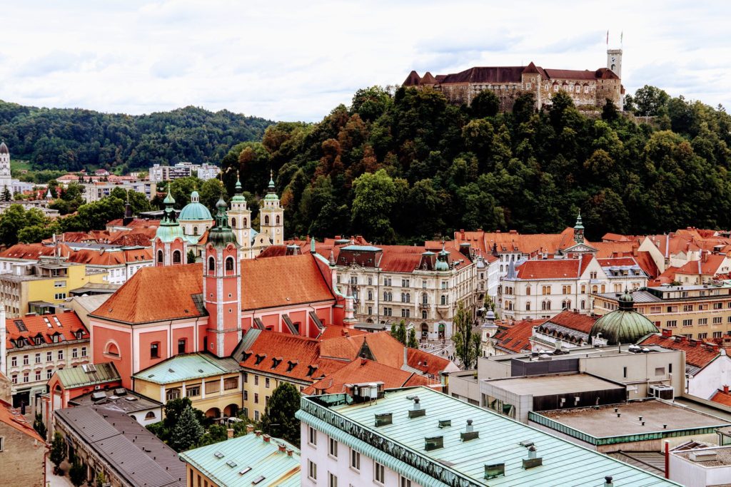 Pogled na Tromostovje in reko Ljubljanico v središču Ljubljane, Slovenija, z zgodovinskimi stavbami in sprehajalci ob reki.