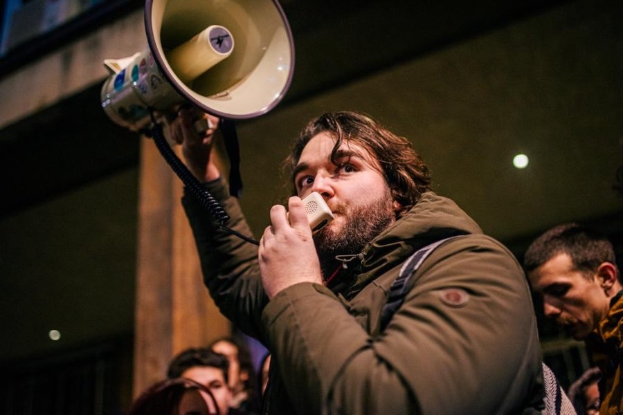 Skupina ljudi, v ospredju je mlad moški, ki govori na megafon.