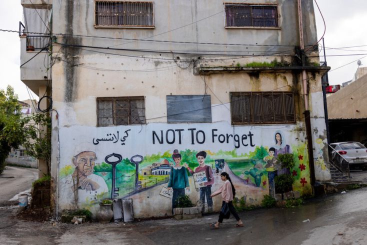 Dekle gre mimo grafitov o nakbi na poškodovani hiši. 31. december 2023, Jenin, Zahodni breg