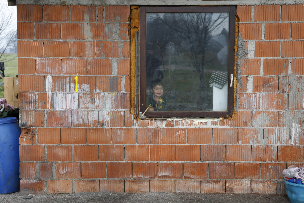 Otrok, ki gleda skozi okno v romskem naselju Goriča vas, kjer še vedno živijo romske družine brez dostopa do vode.