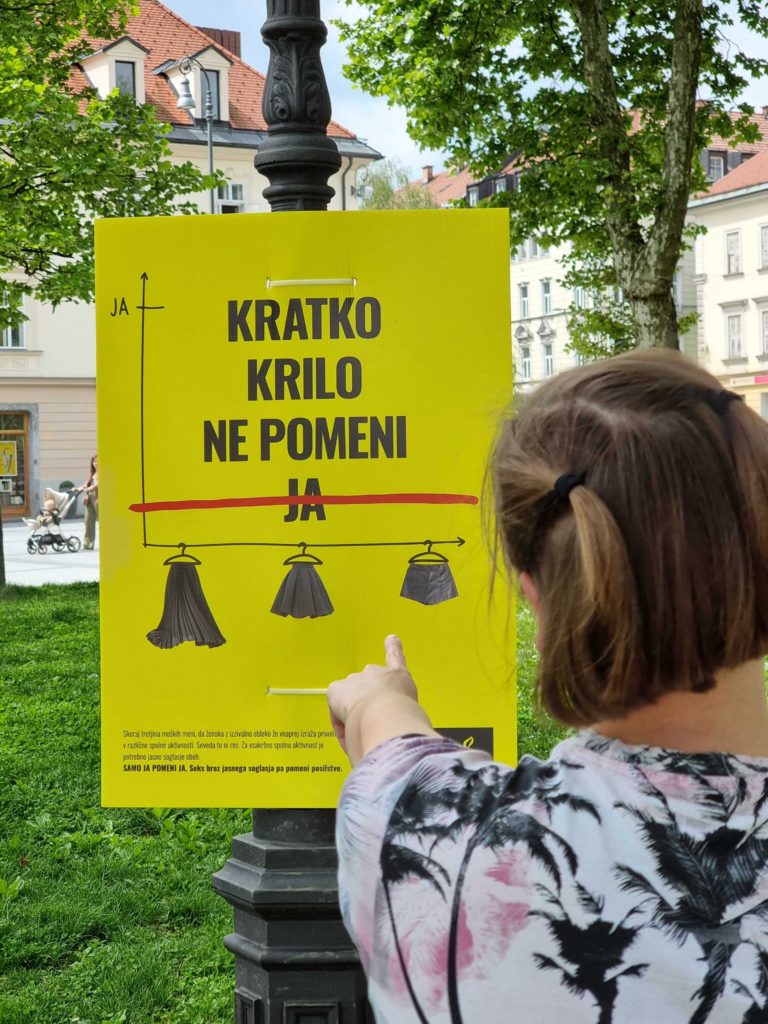 Razstava o soglasju na Poti ob žici 2024. Oseba kaže na plakat na drevesu, na njem piše Samo ja pomeni ja. 