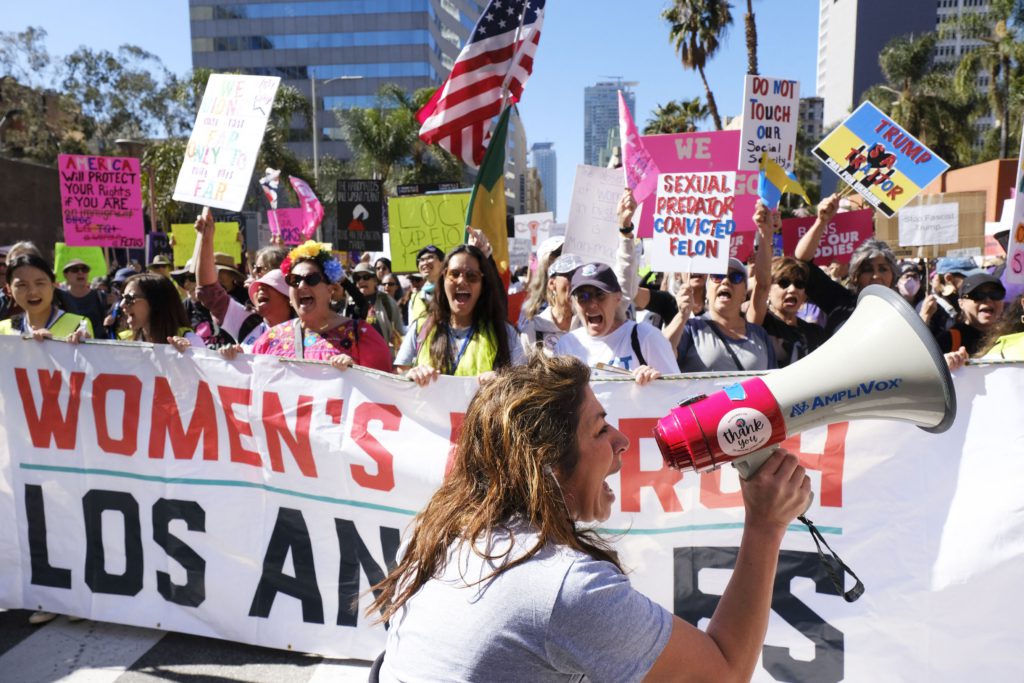 Ženske na protestu s transparentom in megafonom. Protest ob mednarodnem dnevu žensk v Los Angelesu v Kaliforniji 8. marca 2025. 