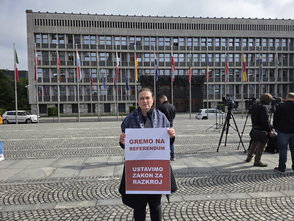 Ženska z napisom "Gremo na referendum. Ustavimo zakon za razkroj" pred poslopjem državnega zbora.