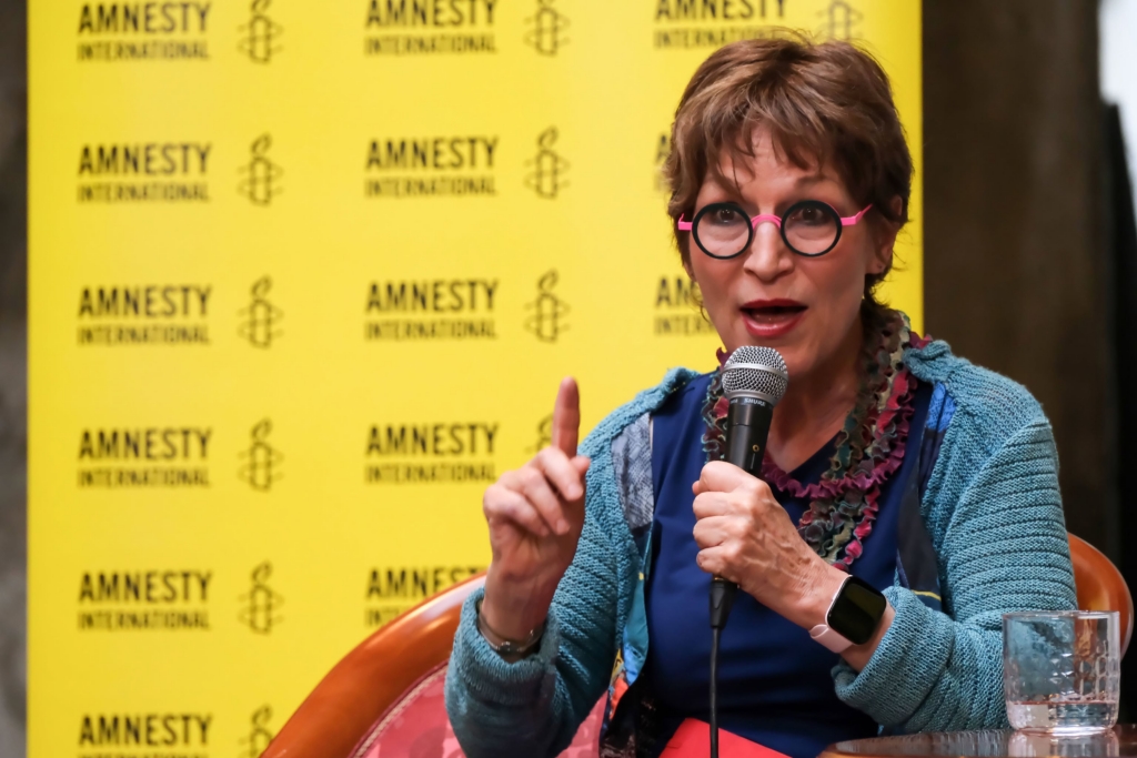 Ženska, ki govori, zadaj logo Amnesty International.